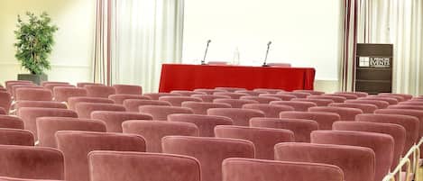 A conference room with rows of red chairs, a podium, and a projector screen.