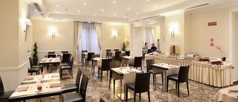 Un comedor de hotel con suelo de mármol, varias mesas, sillas y una barra tipo buffet.