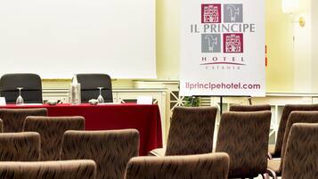 A conference room with a red table, multiple chairs, and a banner for Il Principipe Hotel Catania.