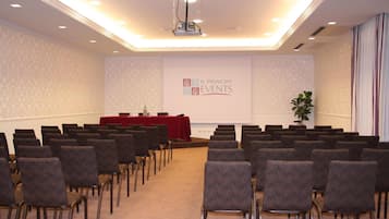 Un salón de conferencias con filas de sillas, un atril y una pantalla para presentaciones.