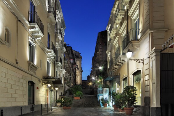 A narrow street with buildings on both sides, featuring balconies and potted plants. - Il Principe Hotel (Catania)