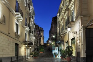 Una stretta via fiancheggiata da edifici, con balconi e piante in vaso.