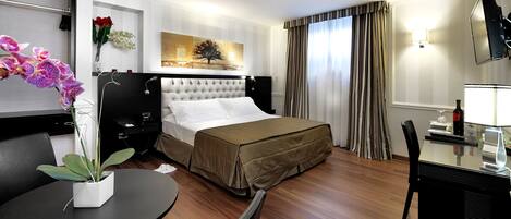 Een hotelkamer met een bed, een eettafel, een stoel, een televisie en een schilderij aan de muur.
