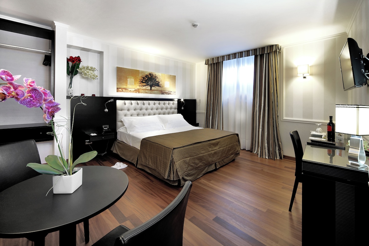 Habitación de hotel con cama, una mesa de comedor, una silla, televisor y un cuadro en la pared.
