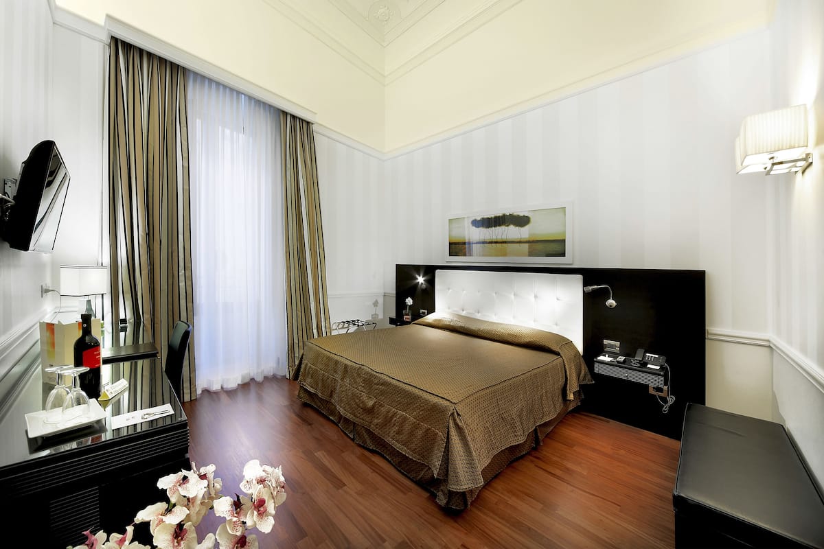 A hotel room with a bed, bedside table, lamp, and a mirror.