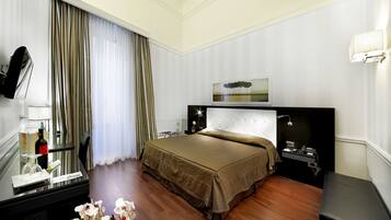 A hotel room with a bed, bedside table, mirror, and a flat-screen TV.