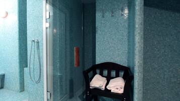 Un bagno con cabina doccia in vetro, una panca in legno con asciugamani e una parete rivestita in piastrelle.