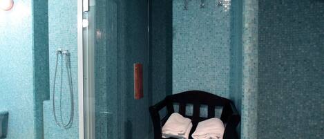 Une salle de bain avec une douche à parois de verre, un banc en bois avec des serviettes et un mur carrelé.