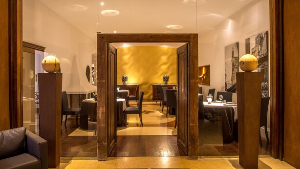 A hotel lobby with a wooden-framed entrance leading to a dining area with tables and chairs. - Central Palace Hotel Federico II (Palermo)