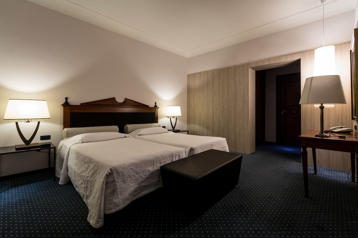 A hotel room with two beds, a desk, a chair, and a nightstand with lamps.