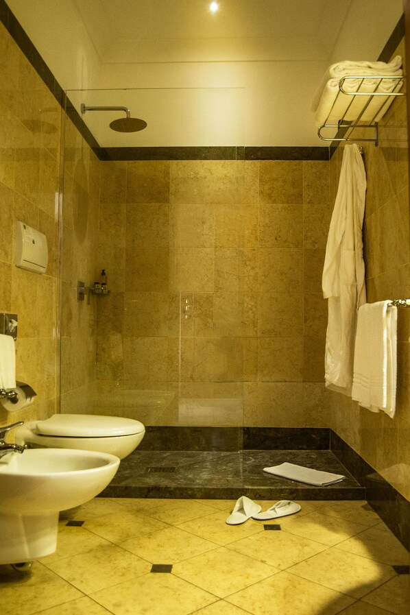 Un baño de hotel con ducha de vidrio, un bidé y un perchero para toallas.