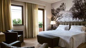 A hotel room with a large bed, a sofa, a chair, and a window with curtains. - Central Palace Hotel Federico II (Palermo)