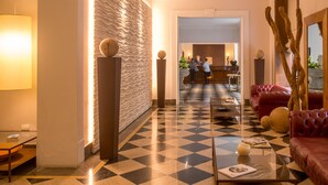 A hotel lobby with a checkered floor, a reception desk, a red leather sofa, and a wall with a textured pattern. - Central Palace Hotel Federico II (Palermo)
