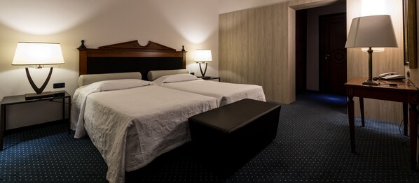A hotel room with two beds, a bench, a desk with a lamp, and a phone. - Central Palace Hotel Federico II (Palermo)