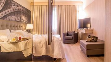 A hotel room with a bed, a desk, a chair, a TV, and a large tapestry on the wall.