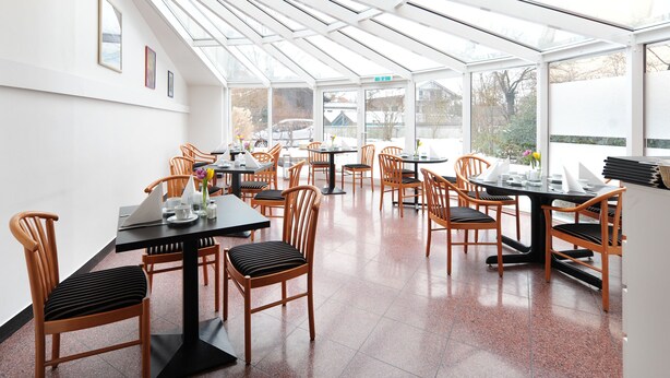 A restaurant with a glass roof, wooden chairs, and tables. - Ambassador Parkhotel (Munich)