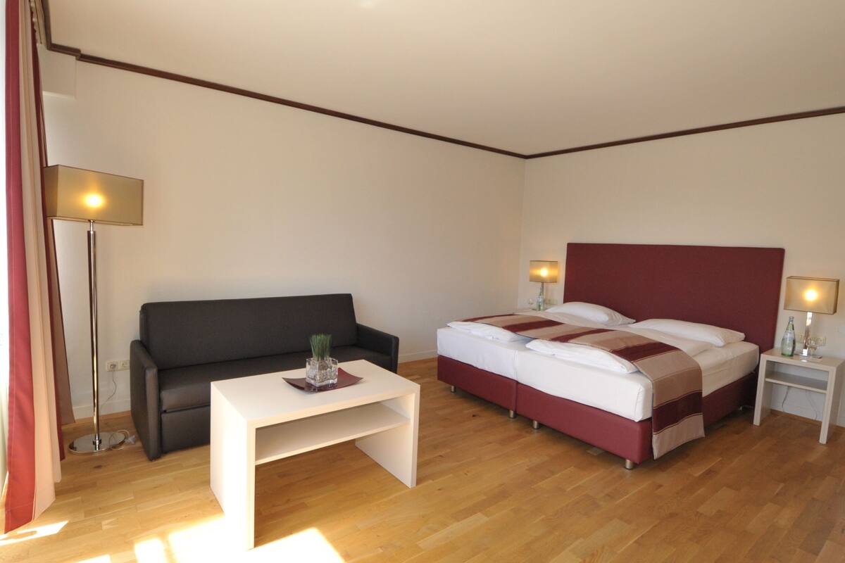 A hotel room with a bed, a sofa, a small table, and a nightstand.