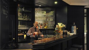 A bar area with shelves of bottles and glasses, a bartender preparing drinks, and stools. - Ambassador Parkhotel (Munich)