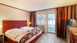 A hotel room with a bed, a TV, a desk, and a window with curtains. - Ambassador Parkhotel (Munich)