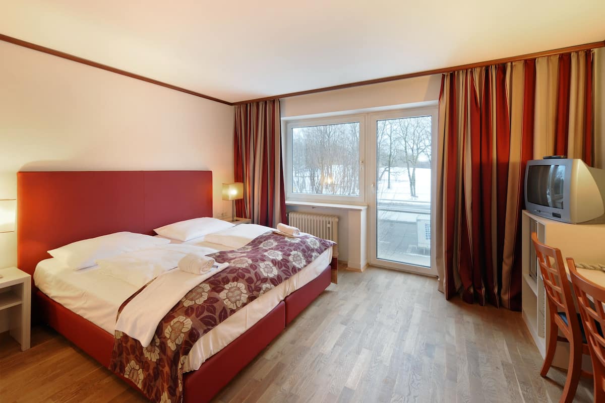A hotel room with a bed, a TV, a desk, and a window with curtains.
