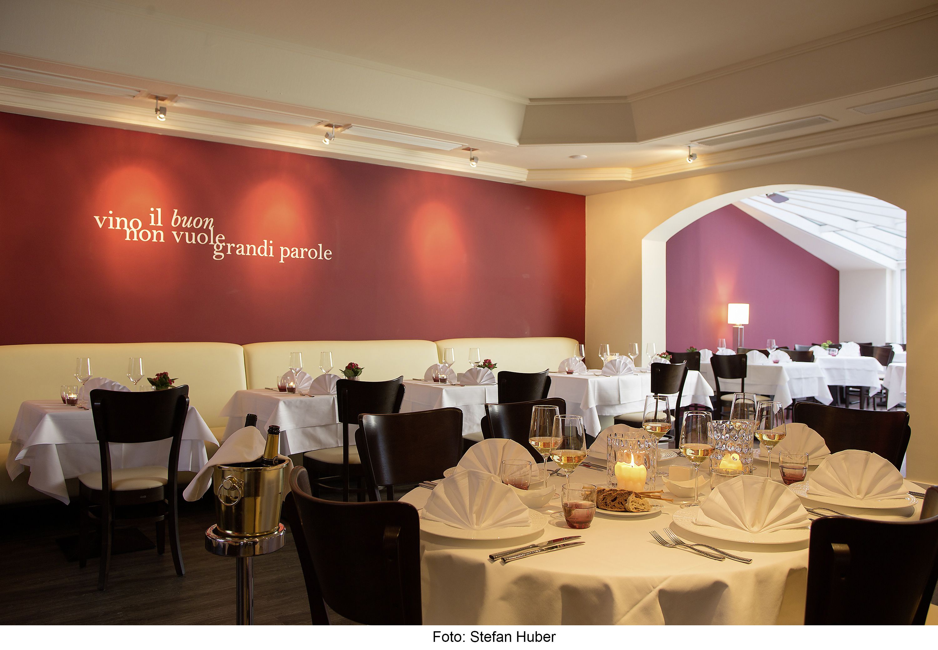 A restaurant with tables set for dining, a champagne bucket, and a wall with a quote in Italian.