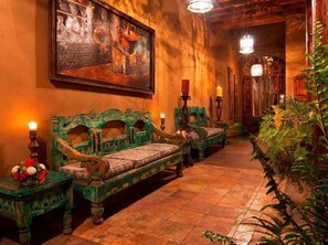 Un corridoio con una panca rivestita in verde, un quadro appeso al muro e un candelabro con candele.