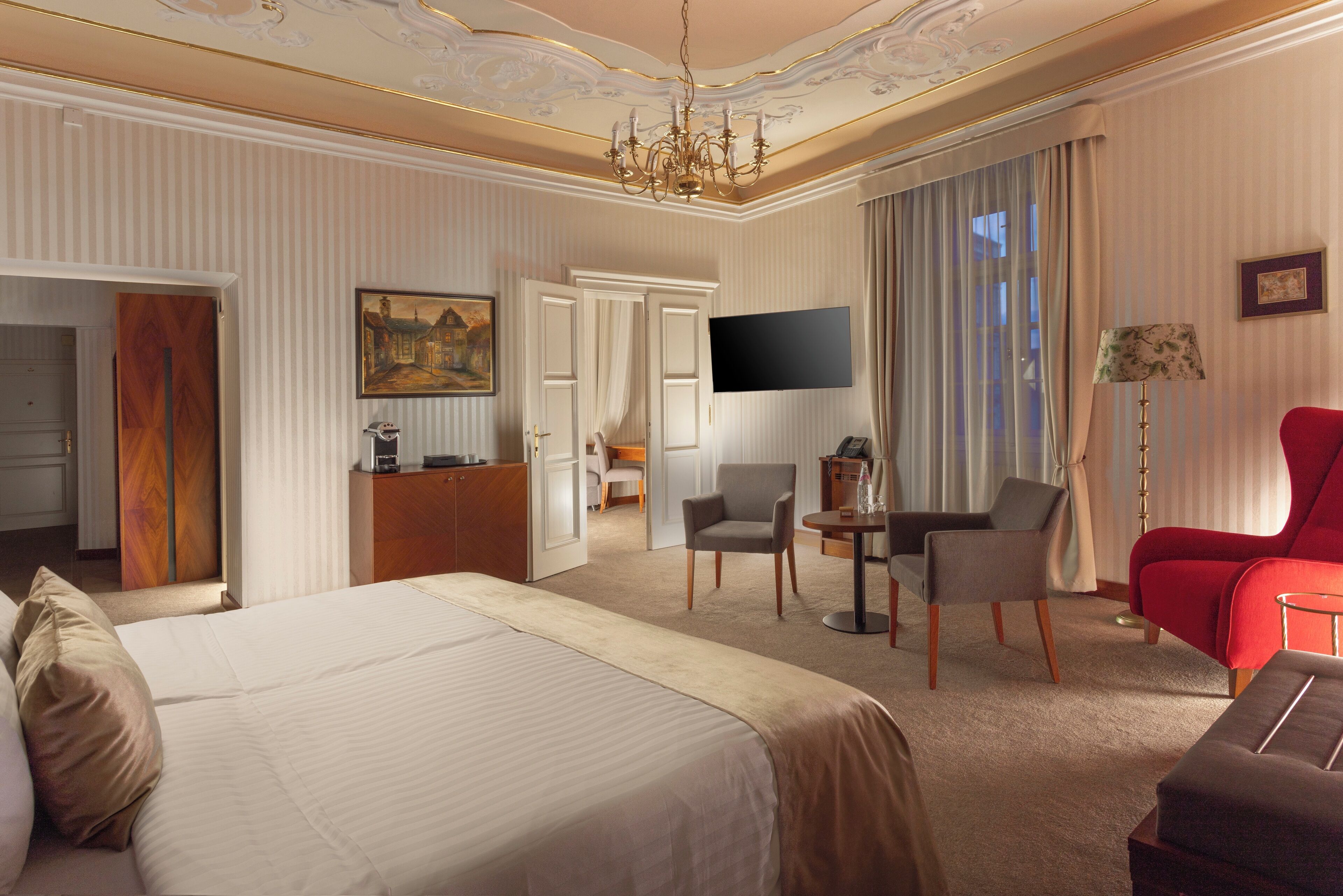 Una habitación de hotel con una cama grande, un escritorio, un televisor y un sillón rojo.