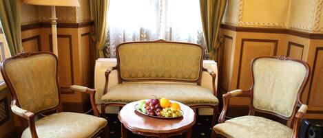 A room with two ornate chairs, a sofa, and a table with fruit.