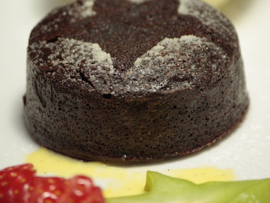Un plato de postre con un pastel volcán de chocolate, una bola de helado de vainilla y fruta fresca.
