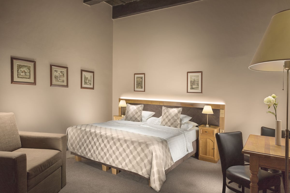 Quarto de hotel bem arrumado com uma cama, uma cadeira, uma mesa e quadros nas paredes.