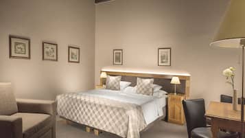 A neatly arranged hotel room with a bed, a chair, a table, and framed pictures on the wall.