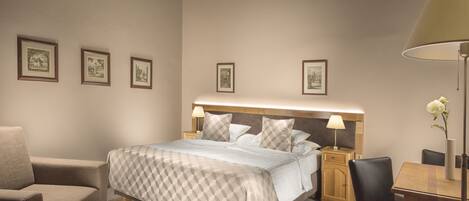 A neatly arranged hotel room with a bed, a chair, a table, and framed pictures on the wall.