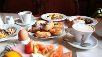 Uma mesa de café da manhã com pratos de croissants, ovos, tomates e café.