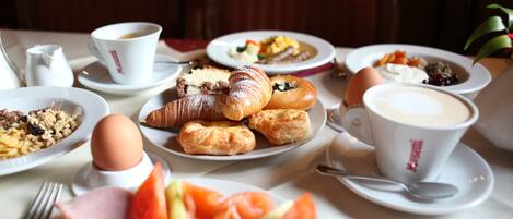A breakfast setting with plates of croissants, eggs, tomatoes, and coffee.
