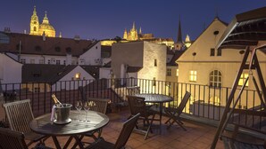 Una terrazza con posti a sedere all'aperto, una bottiglia di champagne e vista su edifici storici al crepuscolo.