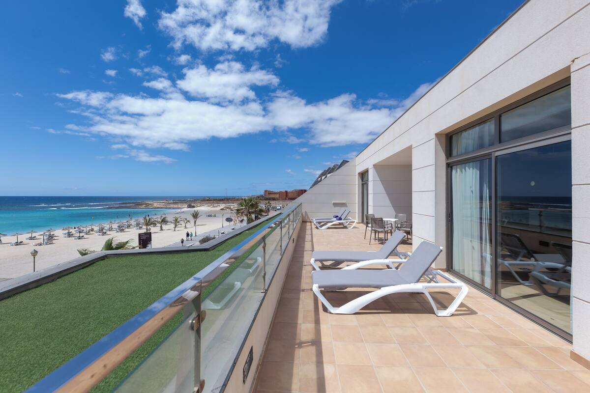 Ein Balkon mit Blick auf den Strand, Liegestühle und einer Glasbrüstung.