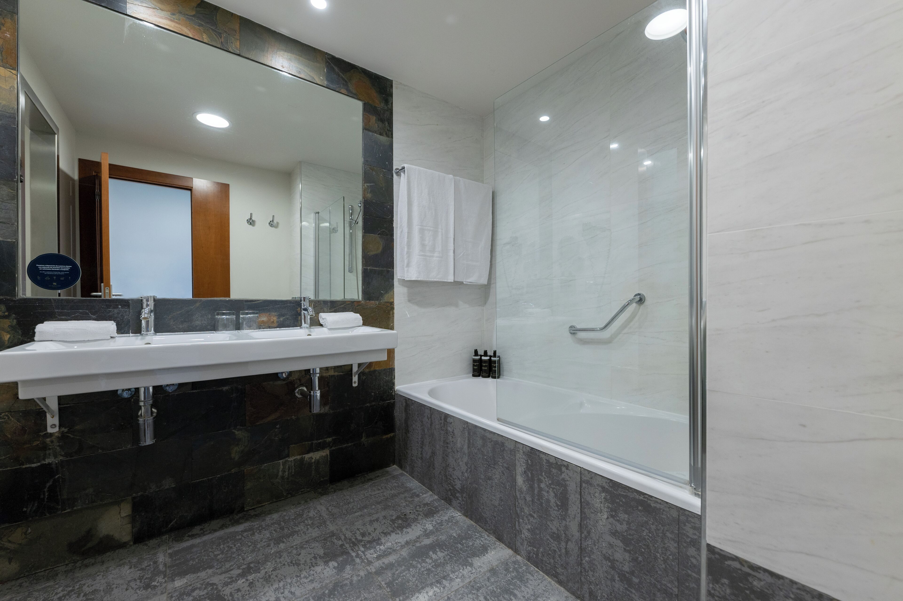 Une salle de bain moderne dotée d’un grand miroir, de deux vasques, d’une baignoire et d’une cabine de douche en verre.