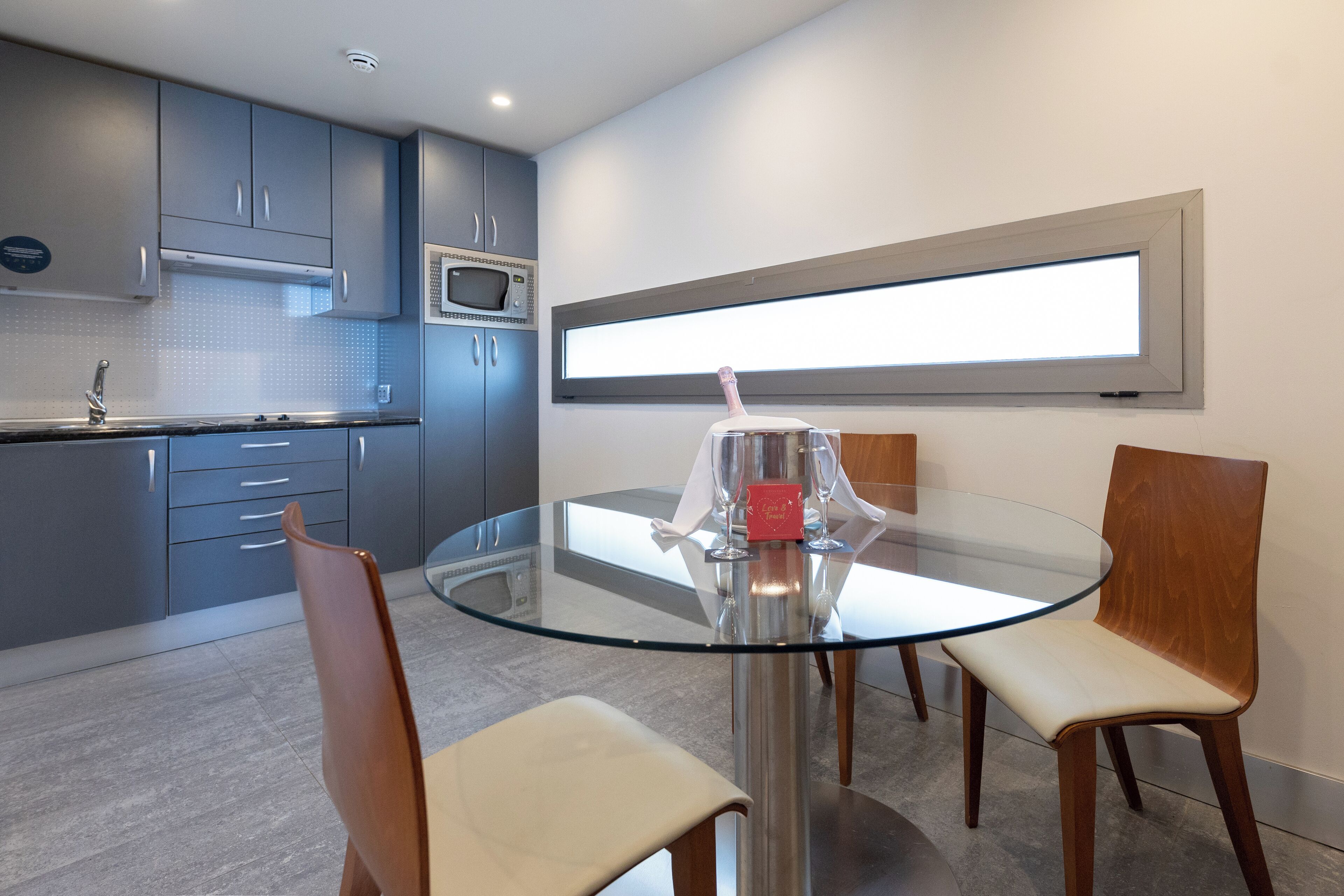 A modern kitchen with grey cabinets, a microwave, and a glass dining table with four chairs.