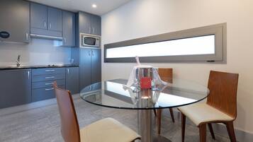 A modern kitchen with grey cabinets, a microwave, and a glass dining table with four chairs.