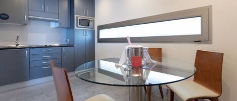 A modern kitchen with grey cabinets, a microwave, and a glass dining table with four chairs.