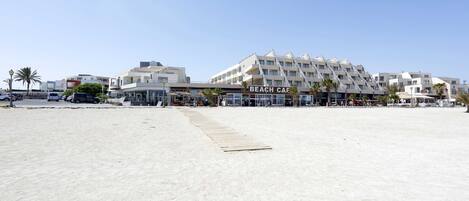 A beachfront hotel with a 'Beach Cafe' sign, a sandy beach, and palm trees.