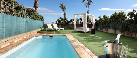A swimming pool with a clear blue water, surrounded by a green fence, and a white canopy structure.