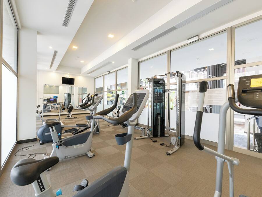 Uma academia moderna com diversos equipamentos de exercício, grandes janelas e um interior limpo e bem iluminado.