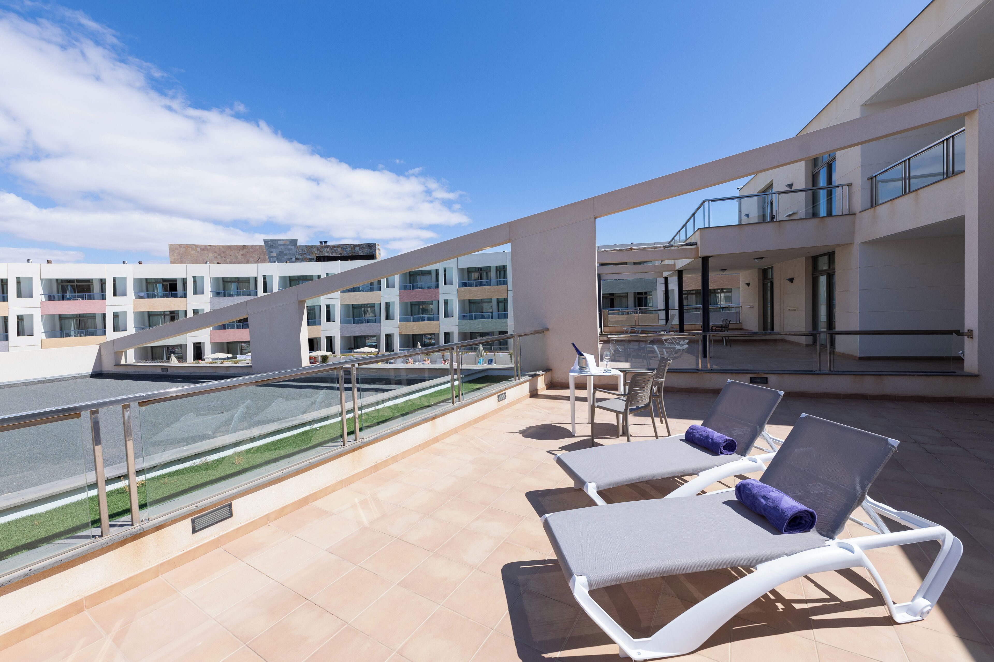 A rooftop terrace with sun loungers, a pool, and a view of the cityscape.