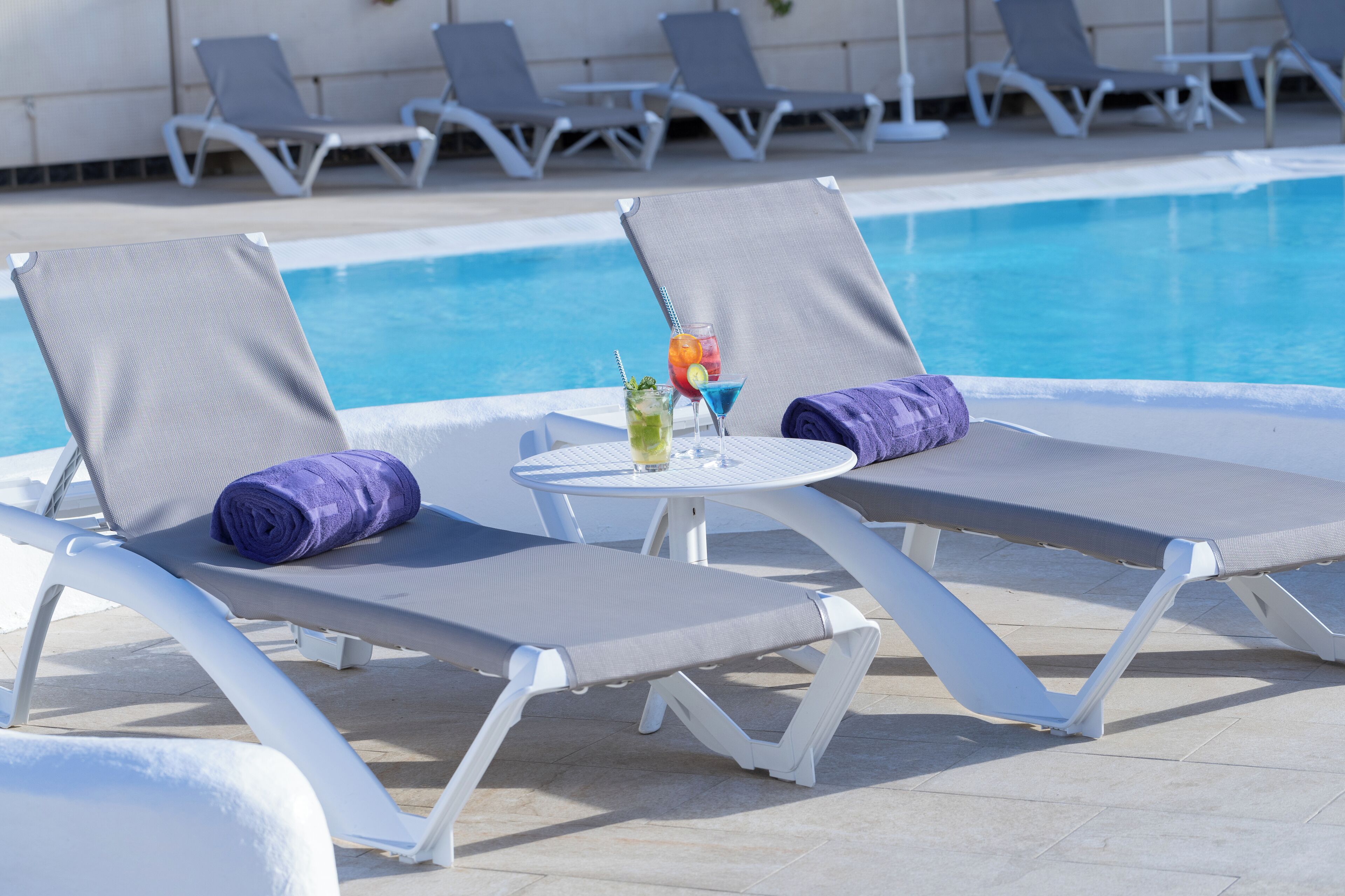 A poolside area with lounge chairs and a table with drinks.