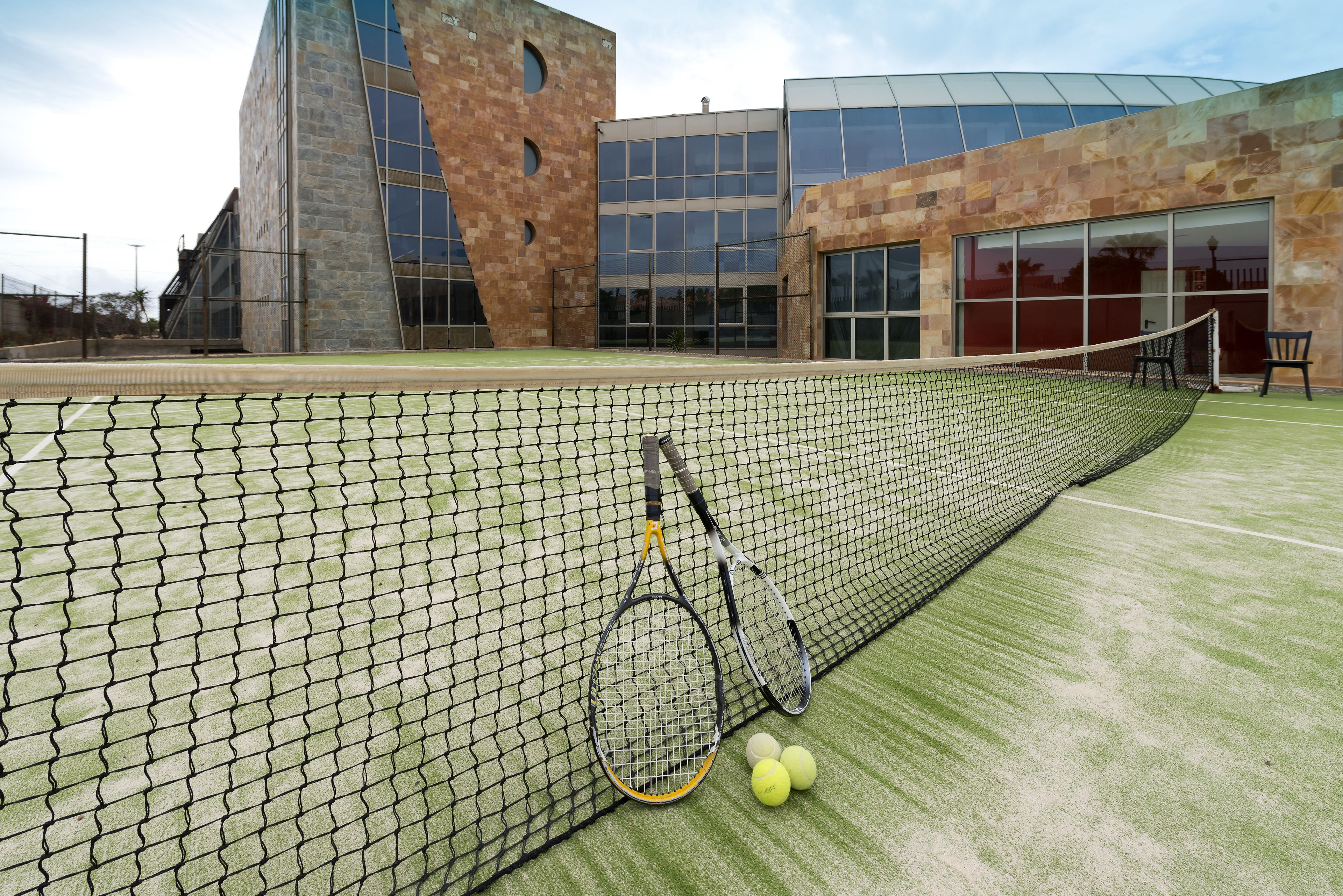 A tennis court with a net, two tennis rackets, and three tennis balls.