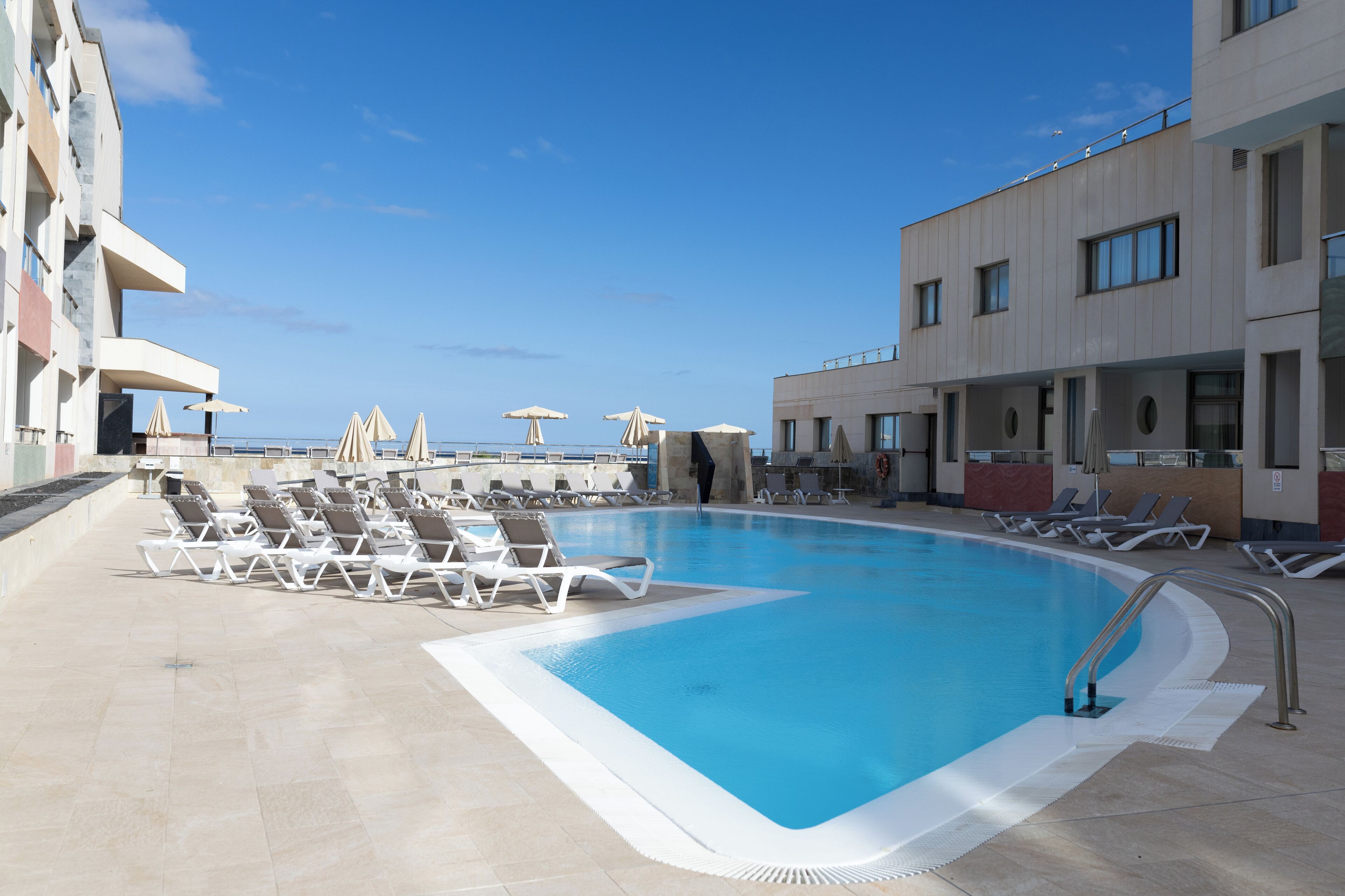A swimming pool with lounge chairs and umbrellas, surrounded by buildings with balconies.