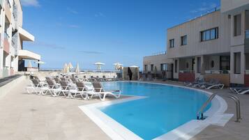 A swimming pool with lounge chairs and umbrellas, surrounded by buildings with balconies.