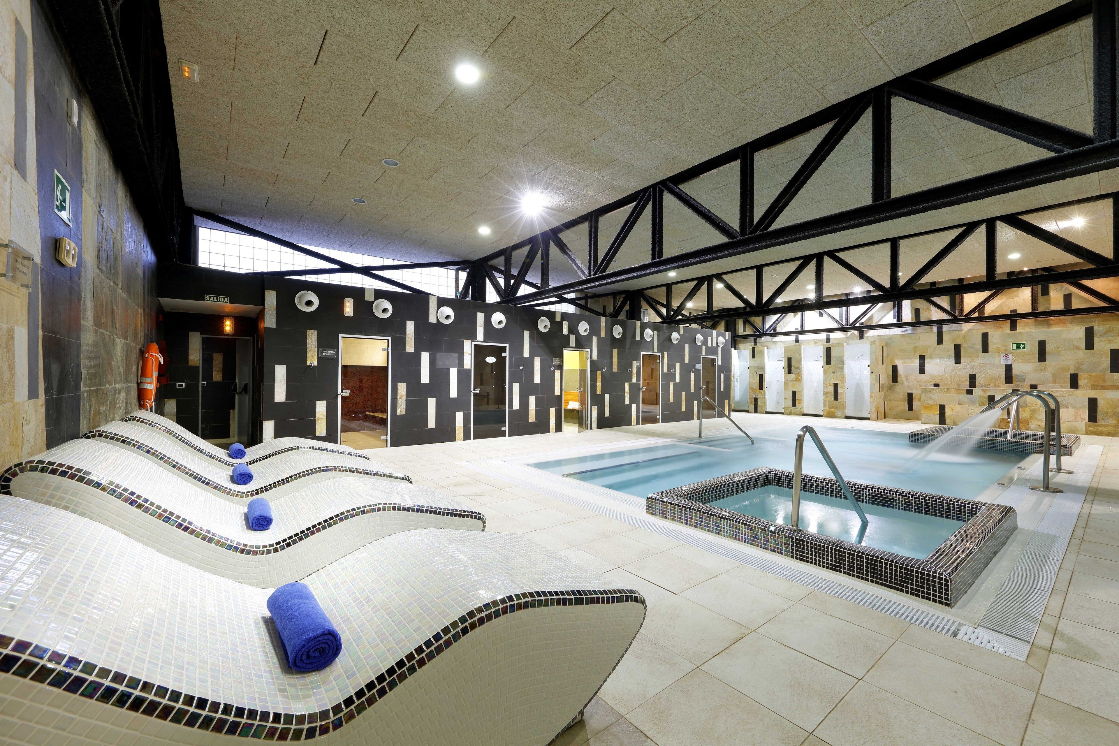 Un área de piscina interior moderna con un jacuzzi, sillones de descanso y una sauna.