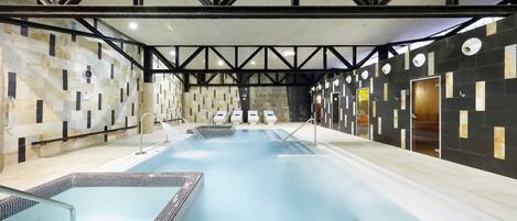 An indoor swimming pool with a modern design, featuring a geometric wall pattern and a high ceiling with truss beams.